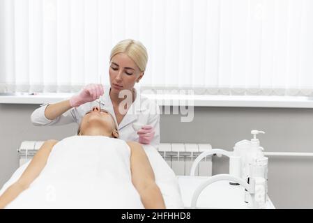 A woman does beauty and spa treatments and applies a moisturizer or mask to her face. Cosmetic procedures. Beautician applies clay mask to woman face Stock Photo