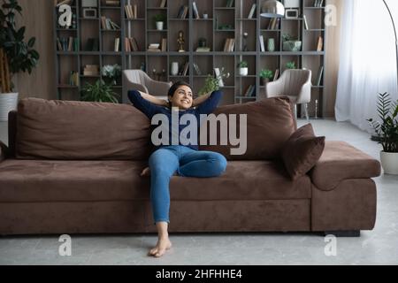 Happy young female Indian homeowner resting on sofa. Stock Photo