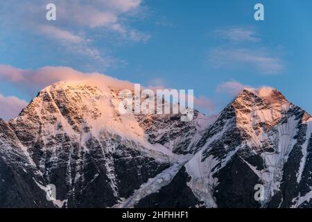 Landscape of high snowy mountains with overhanging glaciers in the sunset rays against a cloudless blue sky Stock Photo