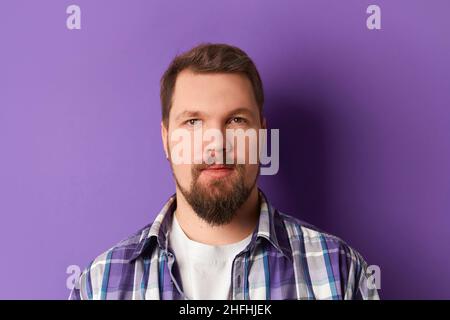Happy bearded man in shirt smiling looking at camera on purple background. Young handsome stylish guy Stock Photo