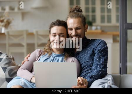 Smiling millennial family couple using computer at home. Stock Photo