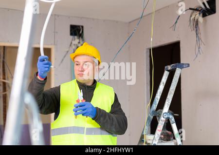 Experienced friendly electrician laying electric wires in building under construction Stock Photo