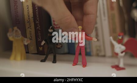 Close up of retro toys of Bremen Musicians standing on a wooden bookshelf with books on the background. Hand puttin small toy figure of Troubadour. Stock Photo