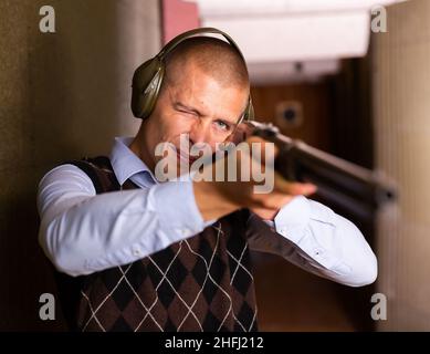 Concentrated man practicing shotgun shooting at firing range Stock Photo