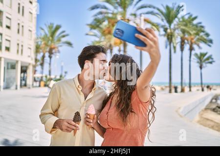 Man and woman couple eating ice cream and kissing making selfie by the smartphone at seaside Stock Photo