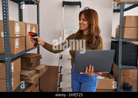 Young latin woman business worker scanning package using barcode reader at office Stock Photo