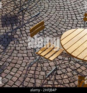 Outdoor German cafe seating with round tables and wooden chairs on cobblestone floor Stock Photo