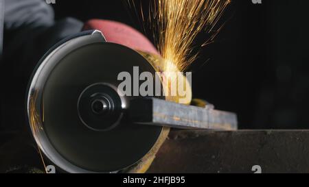 Forge workshop. Smithy manual production. Close up details of sparks, industrial worker using angle grinder and cutting steel. Stock Photo