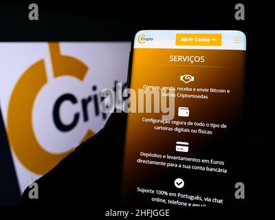 Person holding cellphone with website of Portuguese company Smart Token Lda. (CriptoLoja) on screen with logo. Focus on center of phone display. Stock Photo