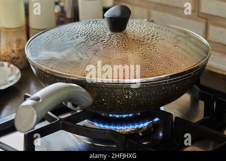 Frying pan on gas stove with the texture of drops on a glass lid with selective focus, background Stock Photo
