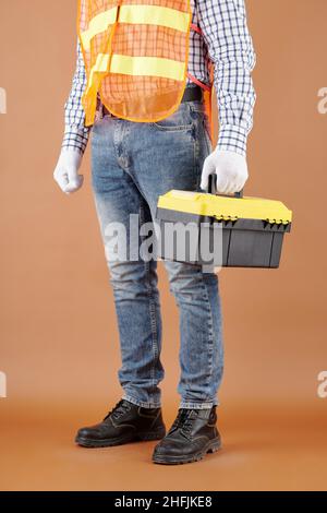 Cropped image of carpenter in jeans and bright vest holding toolbox Stock Photo