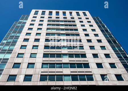 Angled view of a large, window covered apartment building corner against a blue, cloud filled sky Stock Photo