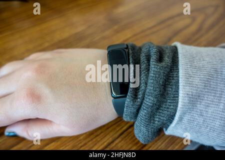 View of a casucasian, female hand with a black fitness tracker on the wrist, set against a wooden table Stock Photo