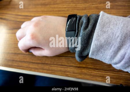 View of a casucasian, female hand with a black fitness tracker on the wrist, set against a wooden table Stock Photo