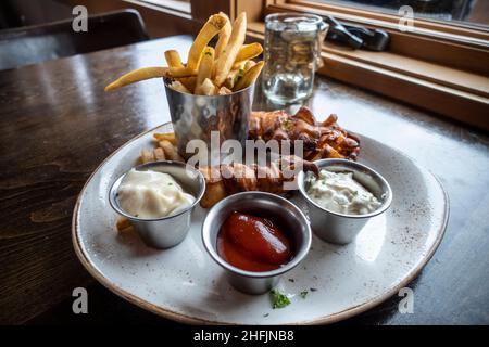 Close up of golden, battered fish fillets with thick french fries on a plate with ketchup, tartar sauce, and ranch dressings inside a restaurant Stock Photo