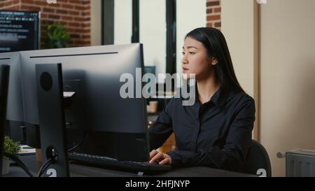 Portrait of asian programer focused on writing code sitting at desk in software development office. System engineer concentrating on creating algorithm for it startup company. Stock Photo