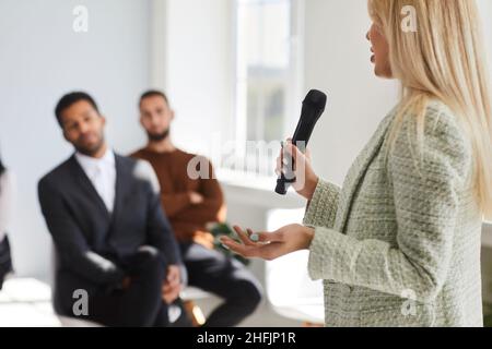 Female business speaker holding a microphone and giving a speech to a diverse audience Stock Photo