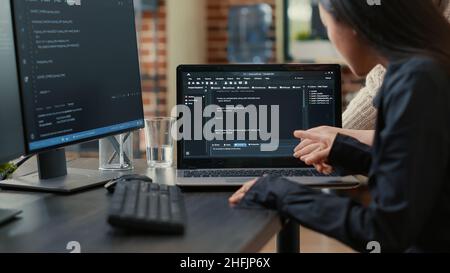 Team of programmers talking about algorithm running on laptop screen pointing at source code while sitting at desk. Software developers collaborating on data coding group project. Stock Photo