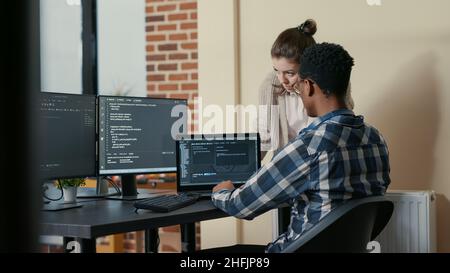 Two programmers doing high five hand gesture at desk with multiple screens running code celebrating successful algorithm. Software developers colleagues enjoying teamwork results in it agency Stock Photo