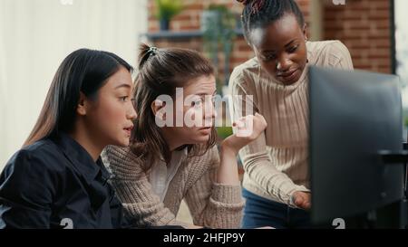 Software engineer pointing at computer screen explaining running code to coworkers brainstorming software ideas in freelance agency. Mixed team of programmers collaborating on it group project. Stock Photo
