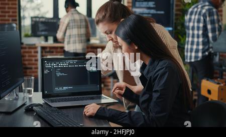 Team of software developers talking about source code running on laptop screen while sitting at desk artificial intelligence server room. Database admins collaborating on data coding group project. Stock Photo