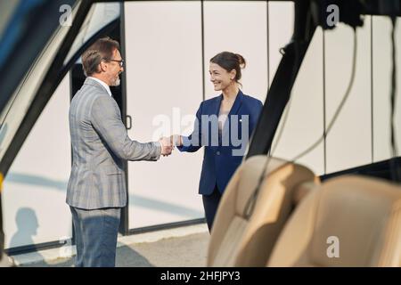 Two joyful elegant entrepreneurs shaking hands outdoors Stock Photo