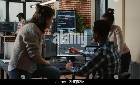 Programer sitting on desk discussing with mixed team of software developers about artificial intelligence innovation. Programmers doing teamwork looking at running machine learning algorithms. Stock Photo