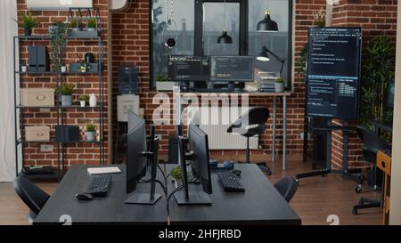 Computer screens on desk in empty software it agency office and computers in background running programming code data algorithms. Neural network servers cloud computing in data room. Stock Photo