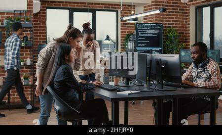 Mixed team of software engineers brainstorming ideas for new code library in front of computer screens compiling algorithms. Diverse app developers collaborating on group project in it agency office. Stock Photo