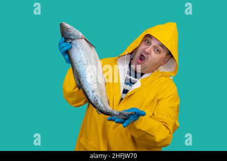 angler in a yellow suit holds a freshly caught fish in his hands. fisherman is surprised by a good catch.  Stock Photo