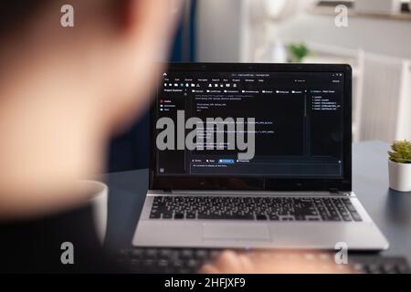 Freelancer writing code on laptop using keyboard. Freelance student programmer working remote developing software. Software coder looking for errors in home office. Code tester debugging. Stock Photo