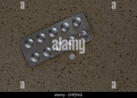 Foil wrapped pills with one white pill extracted on beige background. Stock Photo
