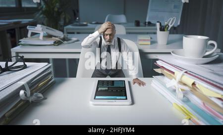 Shocked business executive checking financial reports and statistics on his smartphone, business failure and bankruptcy concept Stock Photo
