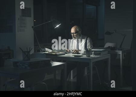 Stressed businessman sitting at desk and working overtime at night, he is having problems with his laptop and he is staring at the computer screen Stock Photo