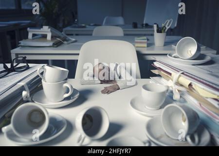 Stressed businessman sitting at desk and working overtime in the office, he fell asleep after drinking many coffees Stock Photo