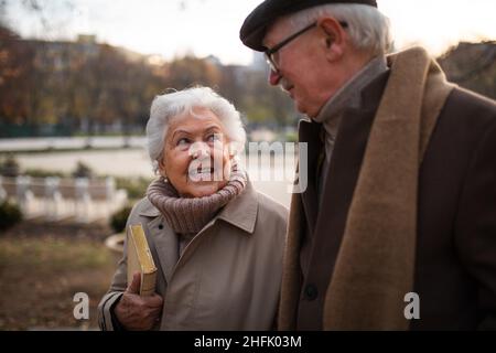 Happy senior friends on walk outdoors in town park in autumn, talking. Stock Photo