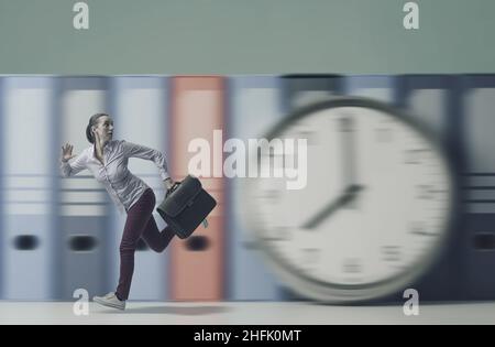 Stressed young businesswoman running fast and huge clock, she is late for work, time management and deadlines concept Stock Photo