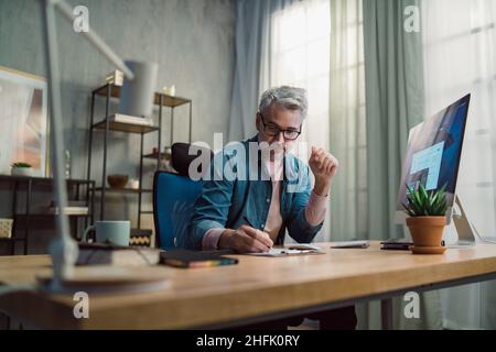 Mature man architect working on computer at desk indoors in office. Stock Photo