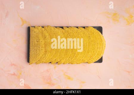 Empty taco shells ingredient. Mexican corn tortilla on black serving slate plate on pink and yellow background. Top view copy space Stock Photo