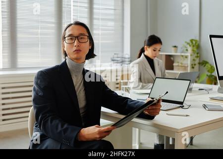 Portrait of successful Asian businessman looking at camera while holding documents in office Stock Photo