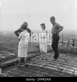 Empress State Building, Lillie Road, Earl's Court, Hammersmith and Fulham, London, 03/07/1961. Two women with a construction worker and manager gathered on the roof of Empress State Building, to watch the final concrete pour. Laing built the foundations and the reinforced concrete frame of the building, work began in November 1959 and ran until July 1961. The group were gathered on the roof to the watch the final pour of concrete to complete the project. Stock Photo