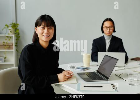 Portrait of young Asian woman looking at camera and smiling while working at table in minimal modern office Stock Photo