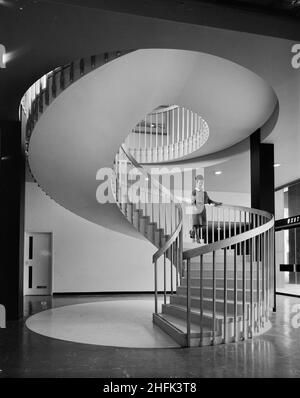 Paternoster Square, City of London, 23/06/1965. A woman walking down a winding staircase in a building at the Paternoster development. Work on the Paternoster development was carried out in a joint venture by John Laing Construction Limited, Trollope and Colls Limited, and George Wimpey and Company Limited. The scheme involved the redevelopment of a seven acre site on the north side of St Paul&#x2019;s Cathedral. The site had been almost entirely devastated during an incendiary raid in December 1940. The development consisted of a series of office blocks, a shopping precinct, an extensive piaz Stock Photo