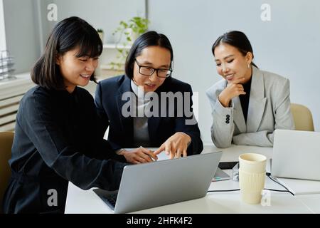 Portrait of Asian business team of three people looking at laptop screen and smiling while meeting in office Stock Photo