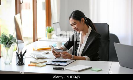 Happy Asian businesswoman is using online shopping application on her smartphone and paying bills by credit card. Stock Photo