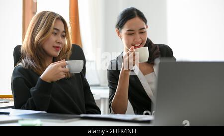 Two Asian female managers are having a hot coffee during a meeting and discussing business plans in the office. Stock Photo