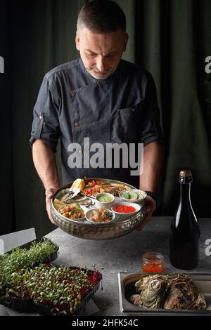 Metal tray with open oysters, raw mussels in the chef's hands. Assorted seafood. Free space for text. Stock Photo