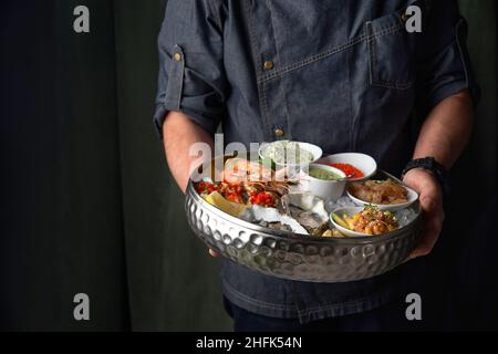 Metal tray with open oysters, raw mussels in the chef's hands. Assorted seafood. Free space for text. Stock Photo