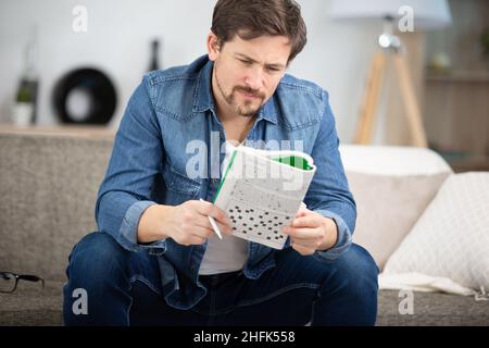 young man sitting on sofa and doing crossword puzzle Stock Photo