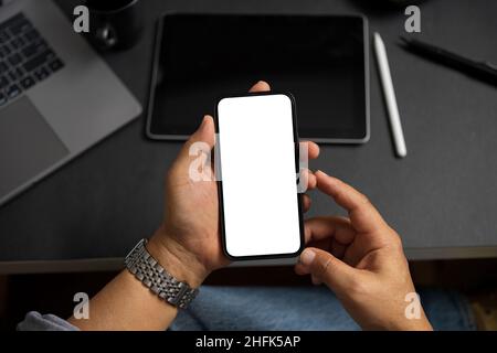 Mockup screen of a modern smartphone in a male or adult man's hands over an office table. Close-up Stock Photo
